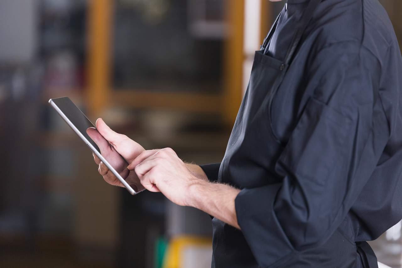 Person in a black apron using a tablet, focusing on the hands and device.