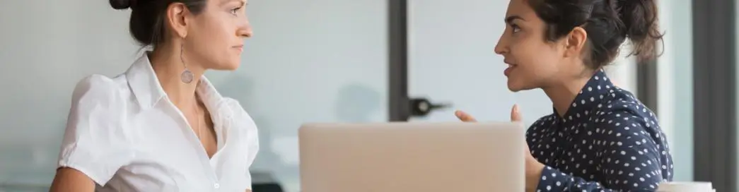 Two women in a serious discussion near a laptop.