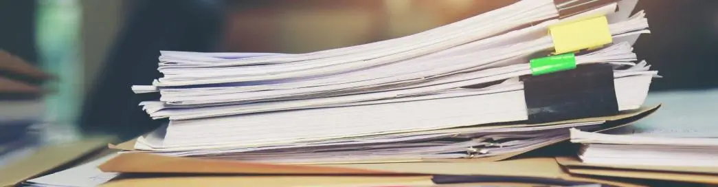 Stack of documents with colored paper clips on a desk.