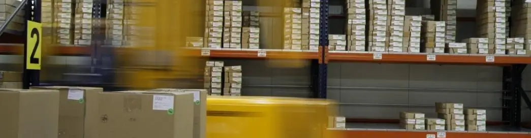 Blurred forklift in a warehouse with boxes on shelves.