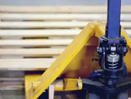 Close-up of a yellow pallet jack next to wooden pallets.