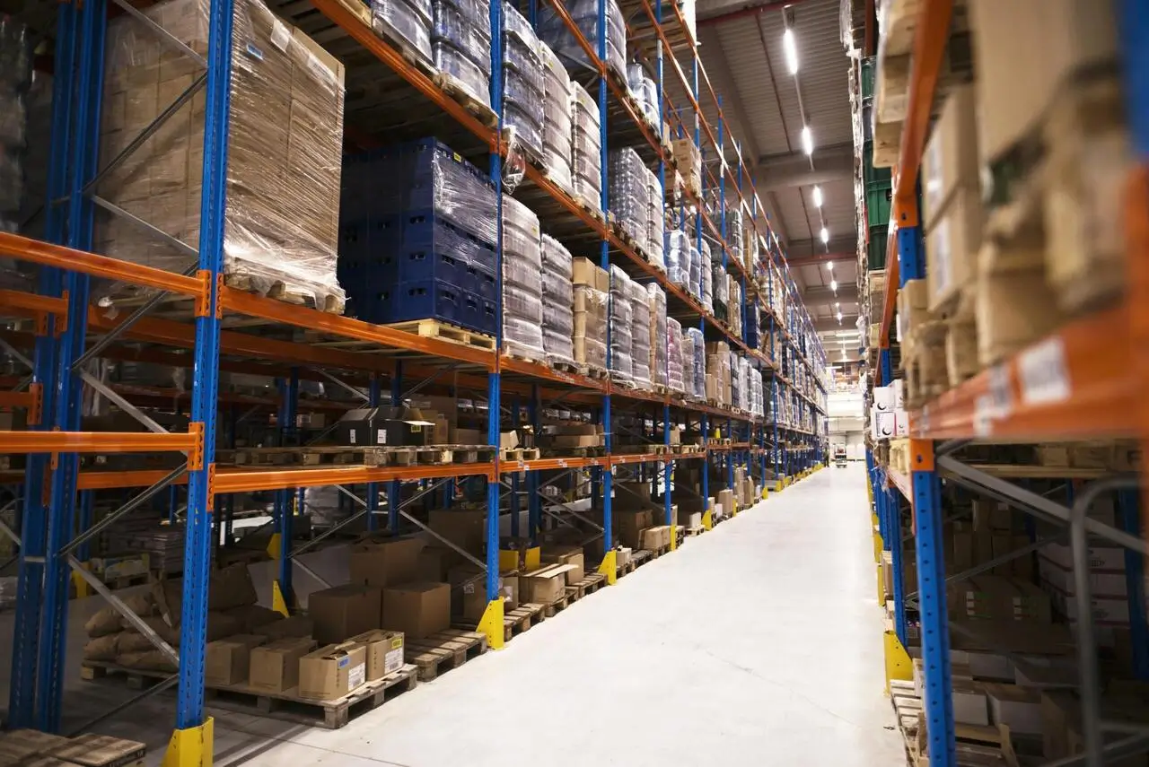 A large warehouse with tall shelves storing pallets of goods in cardboard boxes and plastic wrap.